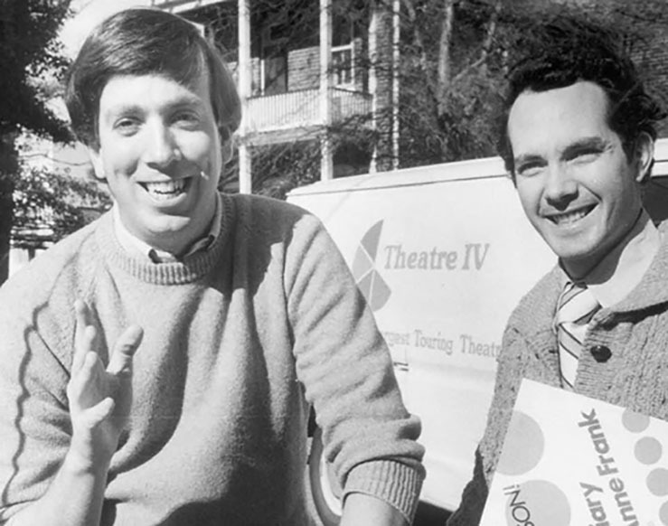 Black and white photo of two smiling men in sweaters standing in front of a van